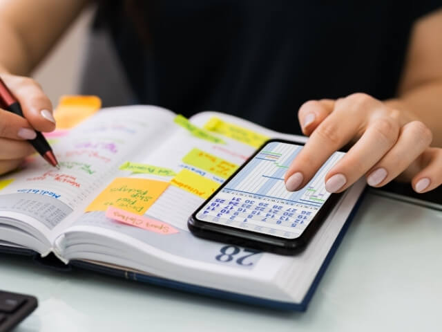 Pessoa com um agenda e um celular sobre a mesa. Organizando sua agenda de atendimentos