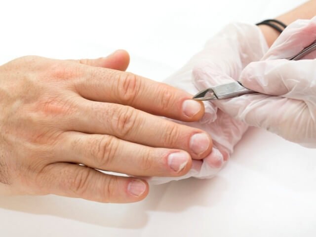 Mãos de uma pessoa retirando cutículas das unhas.